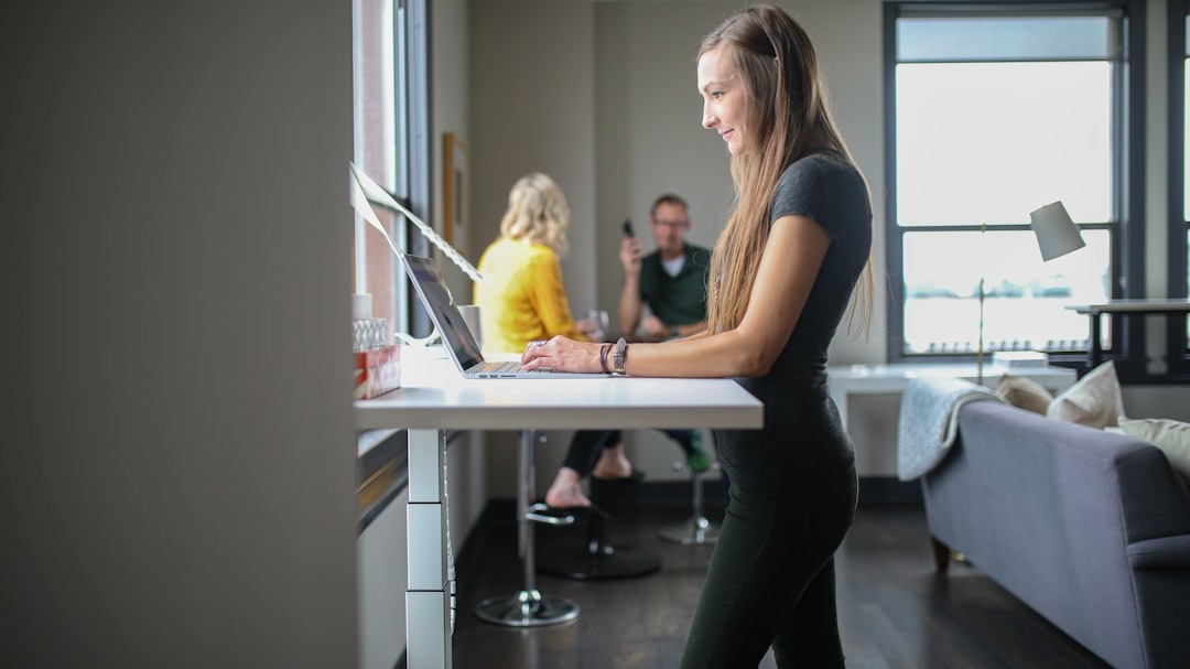Woman typing on a laptop at a standing desk in an office.